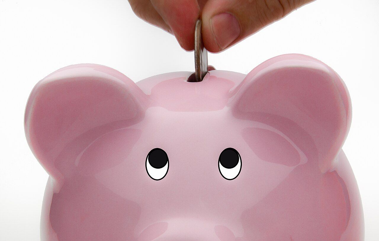 A hand dropping a coin into a piggy bank, illustrating the act of building an emergency fund.